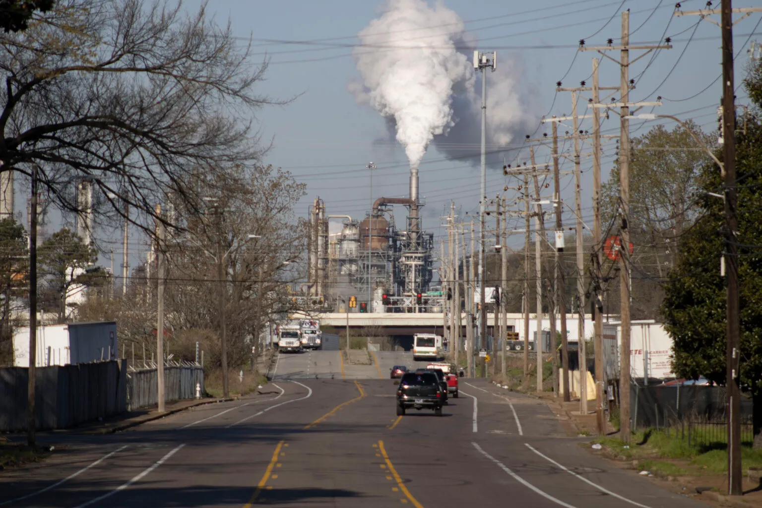 A road in a Memphis residential neighborhood leads toward a large industrial refinery emitting a thick plume of white smoke